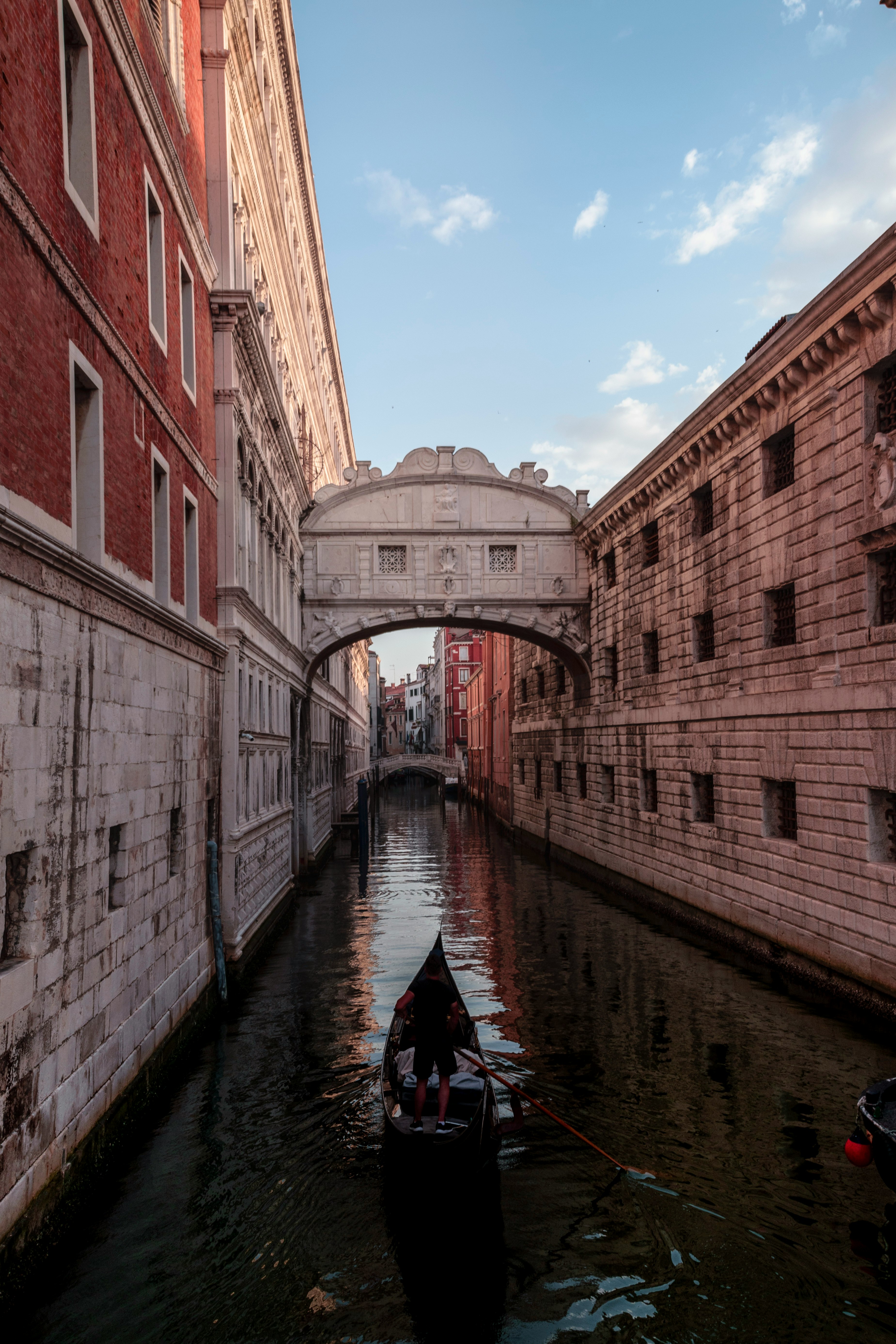 man riding on boat between red and white buildings under blue sky